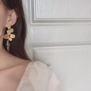 Close-up of matte gold leaf-shaped dangle earrings worn on a model with a soft background