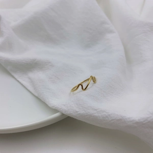 Gold wave pattern minimalist stackable ring on a soft white linen fabric background