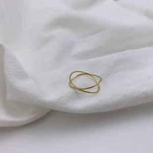 Minimalist double-layered gold wave ring displayed on a soft white linen fabric texture