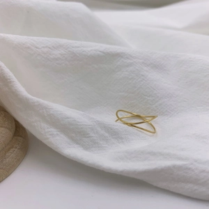 Minimalist double-layered gold ring with a sleek wavy design on white fabric
