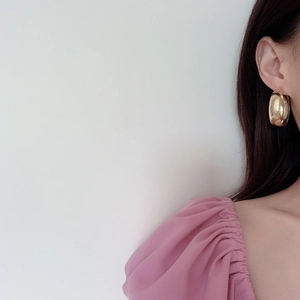 Gros plan de boucles d'oreilles créoles dorées géométriques portées par un mannequin chic