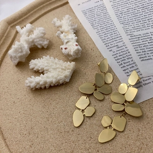 Artistic gold geometric drop earrings on matte tray with decorative white corals