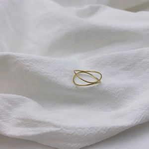 Close-up of a double-layered golden wave ring on a minimalist white linen background