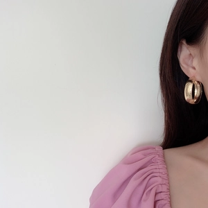Gros plan d'une grande boucle d'oreille créole dorée épaisse portée par un mannequin