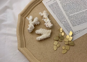 Detail of gold geometric layered earrings on beige tray with decorative white coral