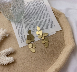 Minimalist geometric gold drop earrings featuring tiered leaf-like metal pendants in matte finish