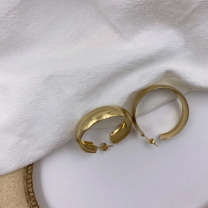 Boucles d'oreilles créoles C larges dorées polies sur une assiette en céramique