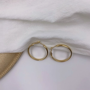 Détails de boucles d'oreilles créoles dorées épaisses avec finition polie sur tissu blanc
