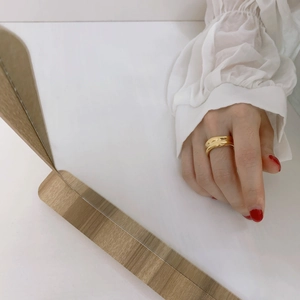Close-up of a wide gold irregular wavy ring worn by a model with red nails and a white shirt