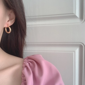 Close-up of model wearing gold twisted hoop earrings with a glossy metallic finish