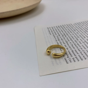 Bague ouverte en acier inoxydable doré poli présentée sur un fond minimaliste chic