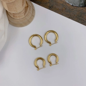 Polished gold geometric hoop earrings in two sizes displayed on white card and wood