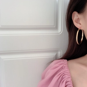 Vue latérale d'un mannequin portant de larges créoles dorées au style minimaliste