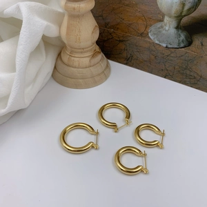 Detail showing two pairs of polished gold hoop earrings in different sizes on white surface