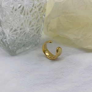 Macro shot of polished irregular wavy gold open ring on white textured fabric background