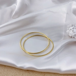 Detail of minimalist gold double loop bracelets resting on white silk fabric with statue
