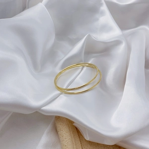 Minimalist double-layer gold polished metal bangles on a white elegant silk background