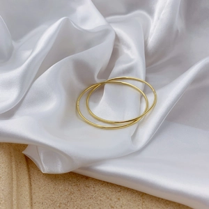 Detail view of two minimalist polished gold bangles on elegant white silk fabric