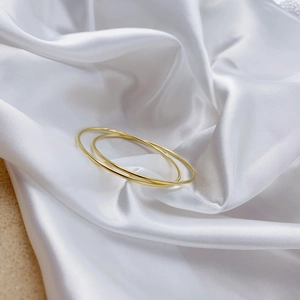 Minimalist double-loop gold metal bracelet on elegant white silk background for women