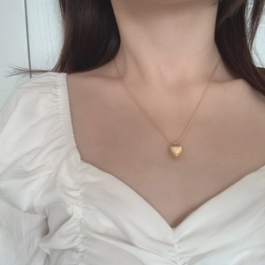 Detailed view of a gold heart pendant necklace worn with an elegant white outfit