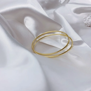 Detailed view of two minimalist polished gold bangles on a luxury white silk background