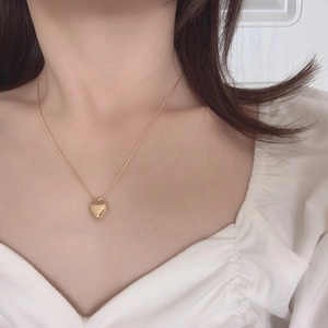 Minimalist gold heart pendant necklace on thin snake chain worn on a model's collarbone