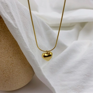 Detail of polished gold heart pendant necklace on minimalist snake chain jewelry