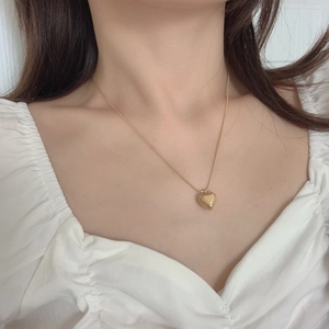 Close-up of a 3D gold heart pendant necklace on a model with white pleated collar