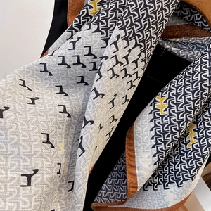 Elegant geometric horse print scarf in grey and orange draped over a wooden hanger
