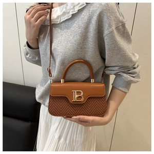 Dettaglio della borsa in pelle caramello e tessuto con logo B dorato su modella