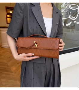 Pochette marron motif serpent avec boucle noeud dorée portée sur blazer gris