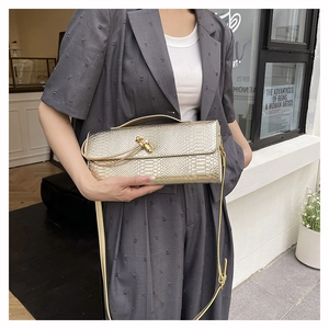 Détail de la pochette dorée à motif serpent, texture métallique et fermoir rotatif chic