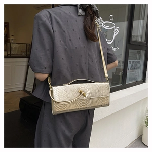 Détail du sac à bandoulière doré à texture serpent avec poignée métallique nouée unique