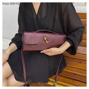 Détail du sac à main bordeaux gaufré serpent avec boucle dorée en forme de nœud chic