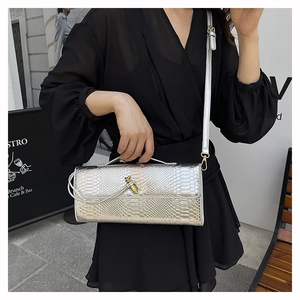 Sac bandoulière serpent argenté avec boucle dorée porté sur une robe noire