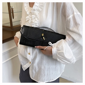 Gros plan sur la pochette noire à effet serpent avec fermoir nœud doré et texture cuir