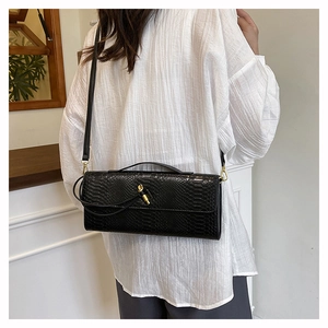 Détail d'un sac bandoulière noir effet serpent avec fermoir rotatif doré sur un mannequin