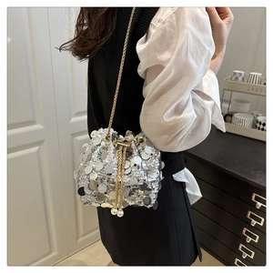Close-up of a silver sequin bucket bag with gold chain and elegant pearl drawstring