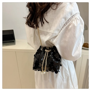 Detail of black sequin bucket bag with gold chain and white pearl drawstring accents