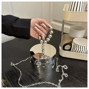 Detalle de bolso cilíndrico plateado con acabado espejo y asa de perlas metálicas