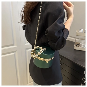 Detalle del bolso cilíndrico verde oscuro con asa de perlas doradas y cadena de metal