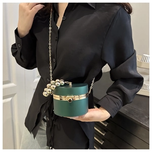 Detalle de bolso cilíndrico verde oscuro con asa de perlas doradas y cadena fina
