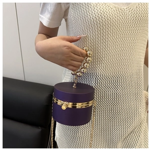 Detalle del bolso de fiesta cilíndrico morado con asa de perlas doradas y cadena