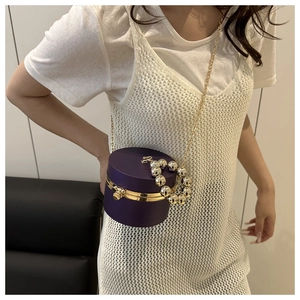 Detalle del bolso de noche cilíndrico morado con cadena dorada y asa de perlas grandes