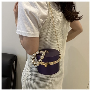 Detalle del bolso de noche cilíndrico morado con asa de perlas y cadena dorada
