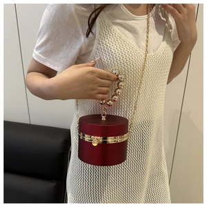 Detalle del bolso cilíndrico rojo con asa de perlas acrílicas y cadena dorada larga