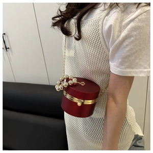 Detalle de bolso de noche cilíndrico rojo con borde dorado y asa de cuentas perlas