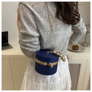 Detalle del bolso de noche cilíndrico azul marino con cadena dorada y asa de perlas