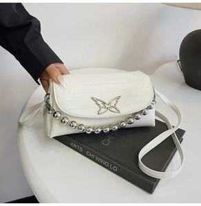 Detail of white crocodile pattern handbag with silver butterfly hardware and bead chain