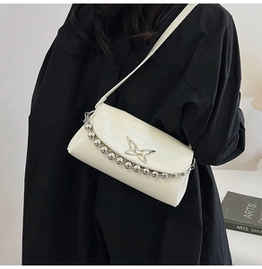Detail of cream white crossbody bag featuring a gold butterfly clasp and beaded edges